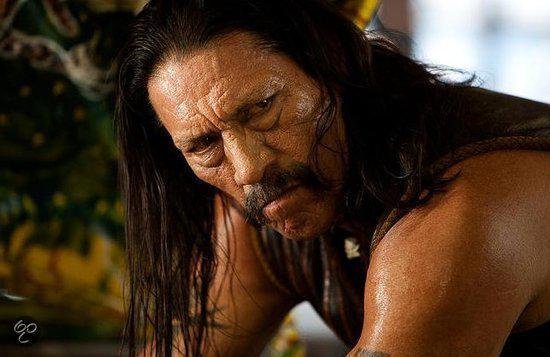 Close-up van Danny Trejo met lang zwart haar, snor en fronsende blik.