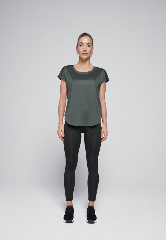 Vrouw staat frontaal, draagt een donkergroen shirt en een zwarte legging, met sportschoenen.