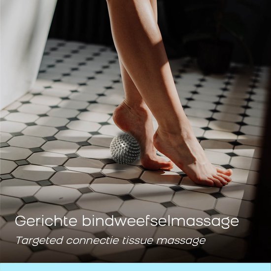 Voeten op een grijze, stekelige massagebal op een betegelde vloer.