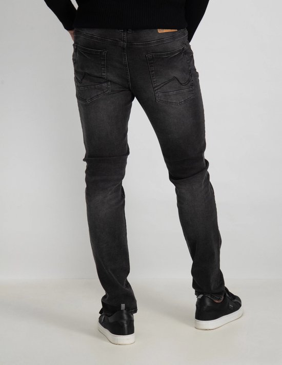 Achterkant van man in zwarte trui, donkergrijze slim fit jeans en zwarte sneakers.