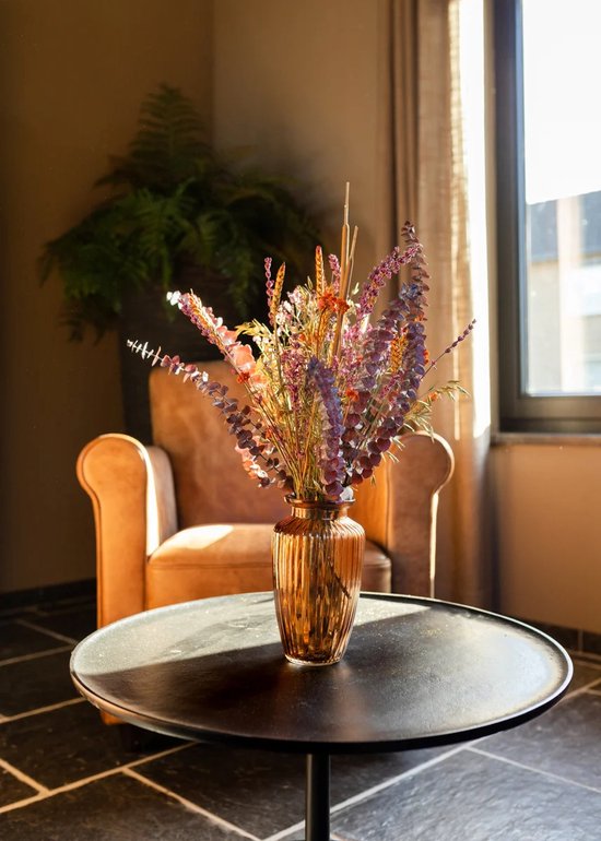 Amberkleurige vaas met een kleurrijk droogboeket op een ronde tafel, zonnig interieur.