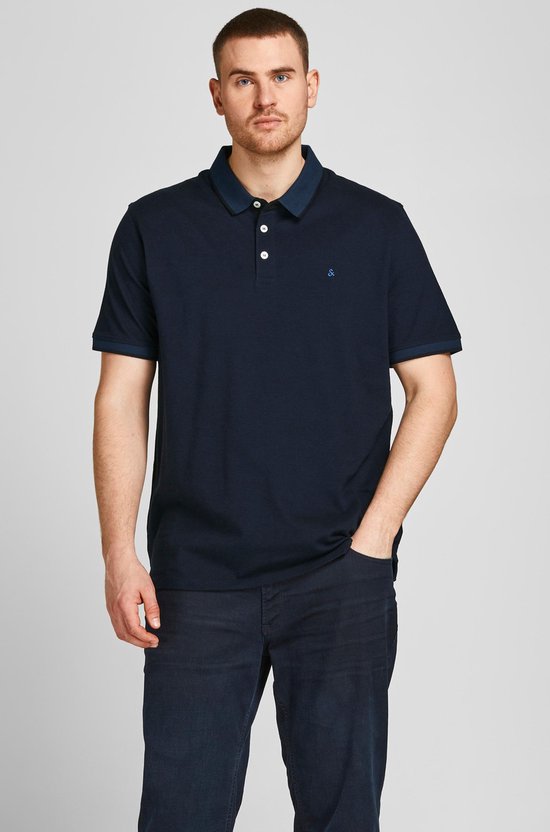 Man in donkerblauw poloshirt met wit geborduurde "&" op borst, navy kraag, drie witte knopen.