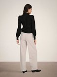 Model op de rug gezien, draagt een zwarte trui en beige wijde broek.