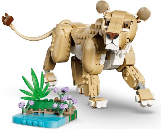 LEGO leeuwin model in beige en bruine stenen, staand bij een blauw waterpartij met groene planten en paarse bloemen.