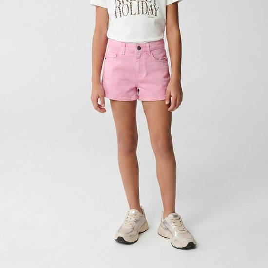 Meisje draagt roze denim shorts met een wit T-shirt en beige sneakers.