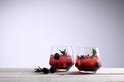 Deux verres à whisky en cristal remplis d'une boisson rouge, de glace, de mûres et de romarin sur fond en bois.
