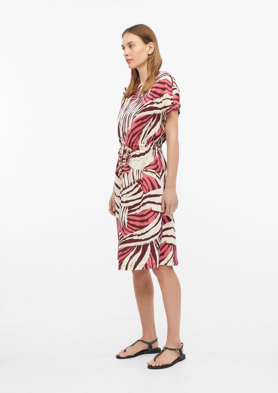 Model draagt een off-white T-shirtjurk met bruine en roze abstracte print, wijde mouwen en ceintuur in de taille.