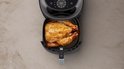Zwarte Philips Airfryer met een hele goudbruine kip in de mand.