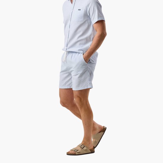 Man in profiel, draagt lichtblauwe gestreepte seersucker pyjamaset.