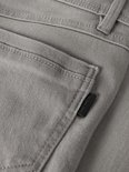 Detail van een grijze jeans met een opgestikte zak en een zwart logolabel aan de zijkant.