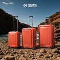 Drie oranje Princess Traveller koffers op een kiezelstrand bij een rivier.