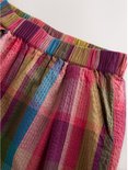 Detail van een geruite broek met wijde pijpen in rood, paars, groen en bruin.