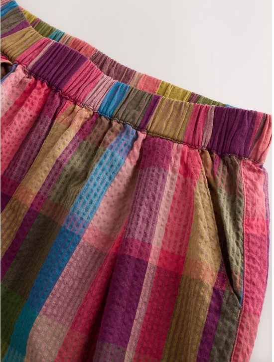 Detail van een geruite broek met wijde pijpen in rood, paars, groen en bruin.
