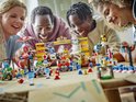 Vier lachende kinderen rond een tafel met LEGO Mario Kart speelgoed, waaronder een kart met Yoshi.