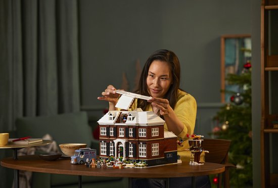 Vrouw bouwt aan een LEGO huis met sneeuw op het dak. De kerstboom is versierd.