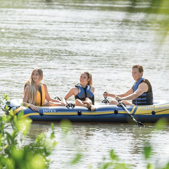 Drie mensen in een blauwe Intex Challenger 3 boot met gele accenten, op het water.