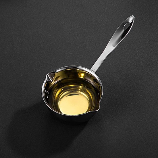 Gouden olie in een roestvrijstalen boterwarmer met een lange steel, op een donkere achtergrond.