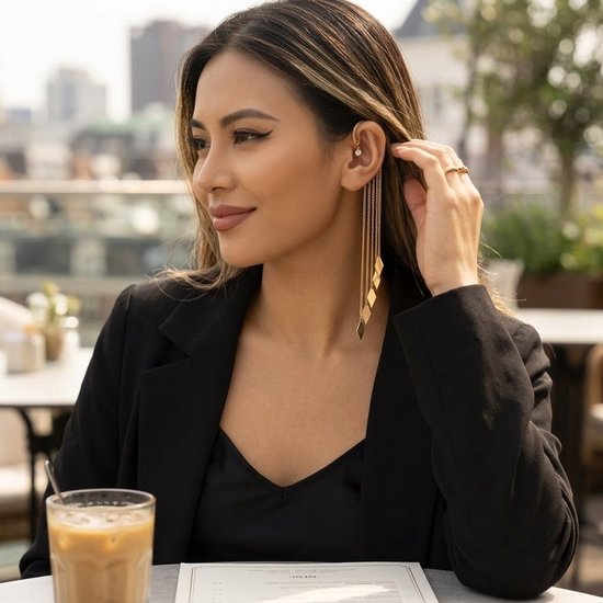 Model draagt een goudkleurige ear cuff met pareldetail en lange kettingen met ruitvormige hangers. Ze draagt een zwarte blazer.