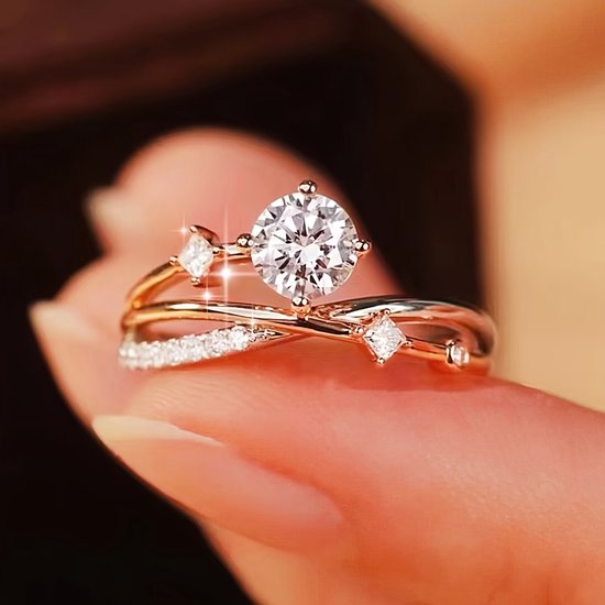 Une bague en or rose avec une grande zircone et de plus petites zircones, portée sur un doigt.