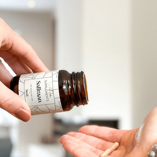 Handen nemen een saffraancapsule uit een bruin supplementenflesje.