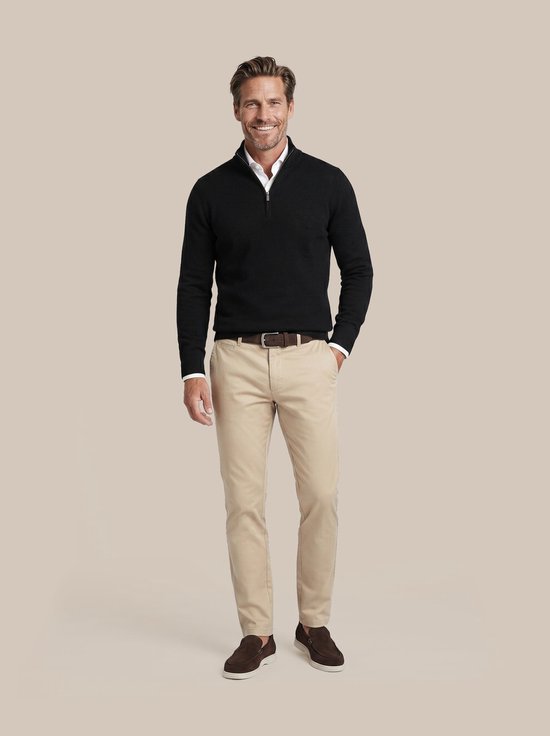 Man met zwarte trui met halve rits, wit overhemd en beige chino broek.