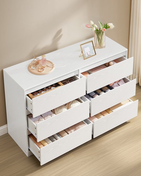 Commode blanche à 6 tiroirs, tous les tiroirs sont ouverts et remplis de vêtements et d'accessoires.
