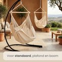 Crèmekleurige hangstoel met houten spreider, aan een zwarte standaard, voor standaard, plafond en boom.