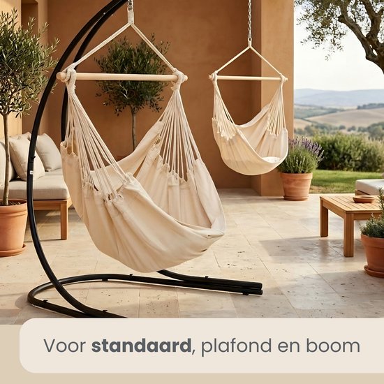 Crèmekleurige hangstoel met houten spreider, aan een zwarte standaard, voor standaard, plafond en boom.