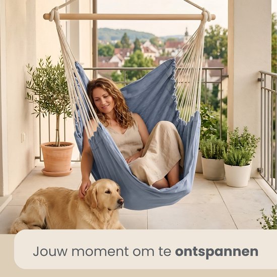 Een vrouw met een hond op een balkon in een blauwgrijze hangstoel.