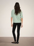 Model met gekruiste armen in een lichtgroene blouse met broderie anglaise, korte mouwen en knopen.