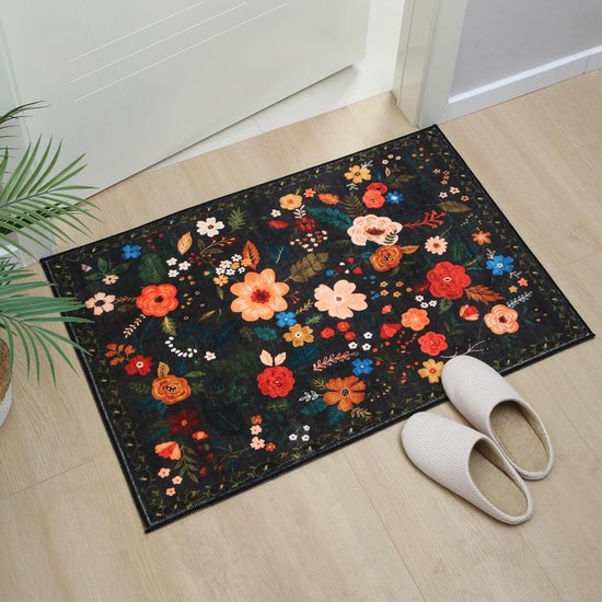 Zwarte deurmat met bloemenprint, bij een witte deur met pantoffels ernaast.