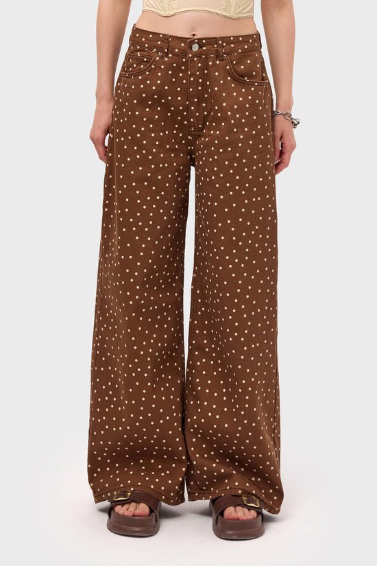 Model draagt een bruine, wijde jeans met witte polkadots en een gele top.
