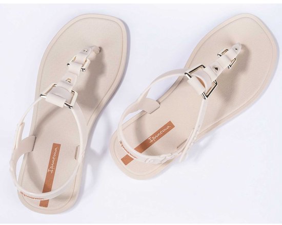 Paar lichtbeige Ipanema slippers, van bovenaf gezien, met enkelbandjes en banden over de wreef met gouden gespen.