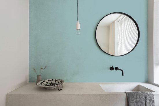 Badkamer met een lichtblauwe muur, betonnen wastafel en zwarte kraan.