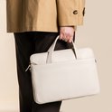 Man in beige jas en donkere broek draagt een off-white laptoptas.