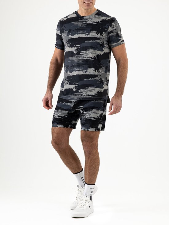 Man in een grijs en zwart camouflage sportshirt en short, met witte sportsokken en schoenen.