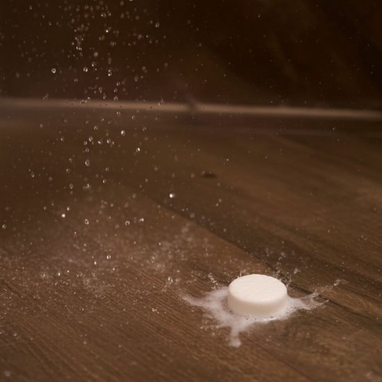 Een witte shower steamer op een houten douche vloer met opspattend water en schuim.