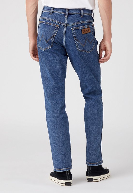 Blauwe Wrangler jeans met bruin leren label op de achterkant, gedragen door een man.