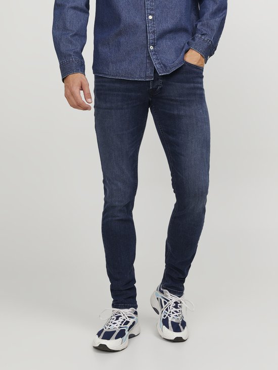 Blauwe skinny jeans gedragen door een man met spierwitte sneakers en een spierwitte denim blouse.
