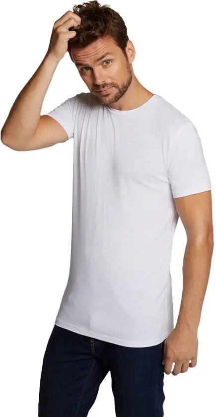 Een man in een wit T-shirt met ronde hals en een spijkerbroek, krabt aan zijn hoofd.
