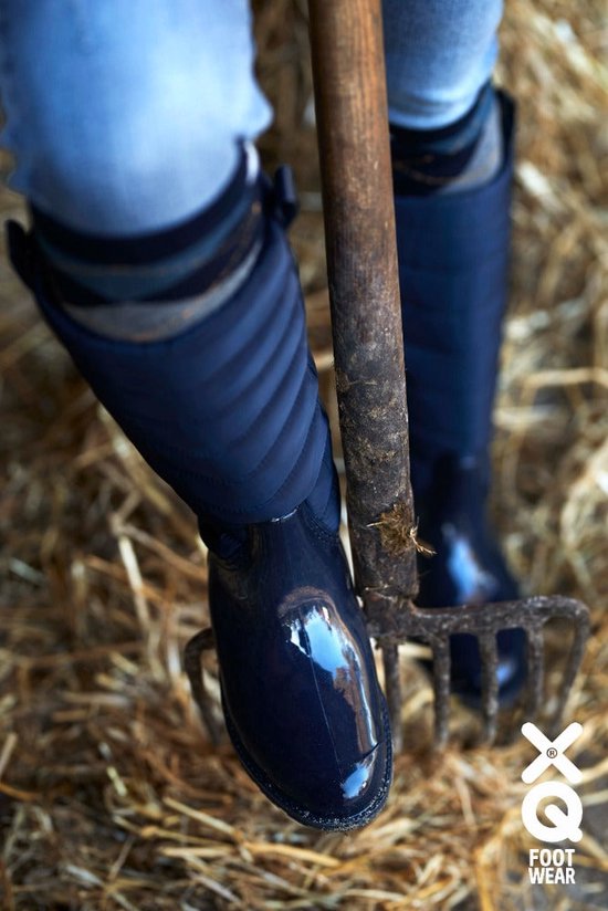 Gedetailleerde close-up van de navy, gewatteerde hoge regenlaarzen van een vrouw, gedragen in een boerderijomgeving.