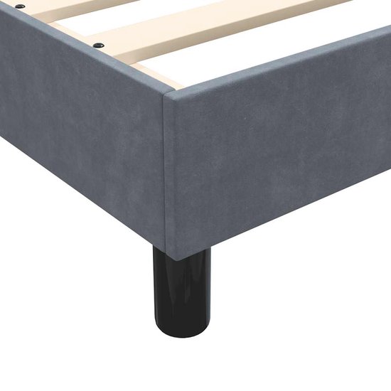 Close-up van de hoek van een donkergrijs fluwelen boxspringframe met een zwarte poot.