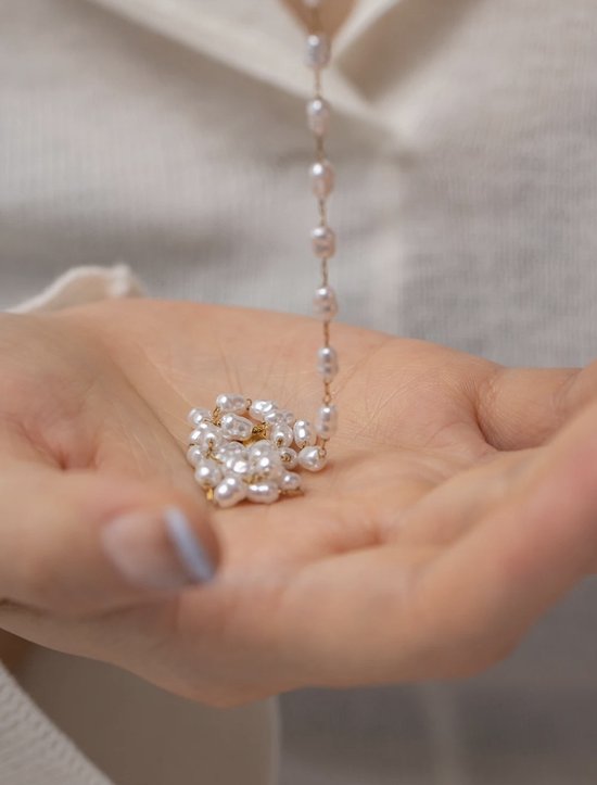 Hand die een opgevouwen gouden ketting met witte parels vasthoudt.