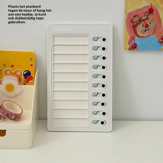 White reusable chore board with a grid for tasks and checkmarks, displayed on a desk next to a small drawer organizer with stickers.