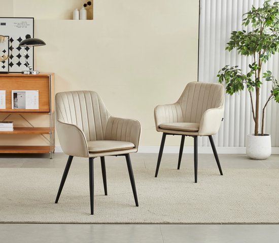 Deux chaises de salle à manger en velours beige avec accoudoirs, côtes verticales et pieds noirs dans un salon.