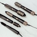 Vijf zwarte Remington föhnborstels met gouden accenten en verschillende opzetborstels, liggend op een marmeren ondergrond.