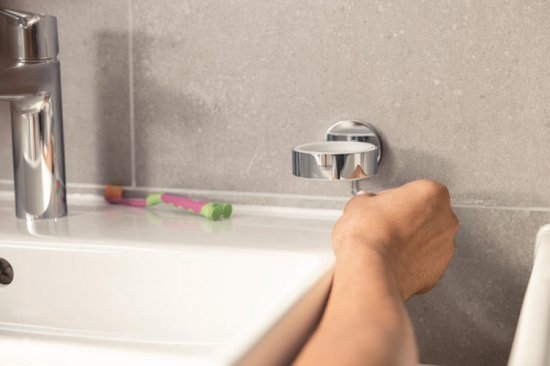 Une main tourne un support sur un support mural, à côté d'un lavabo blanc.