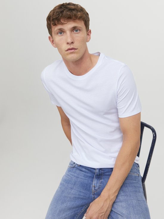 Man zit op een stoel met een witte T-shirt met ronde hals en blauwe jeans.