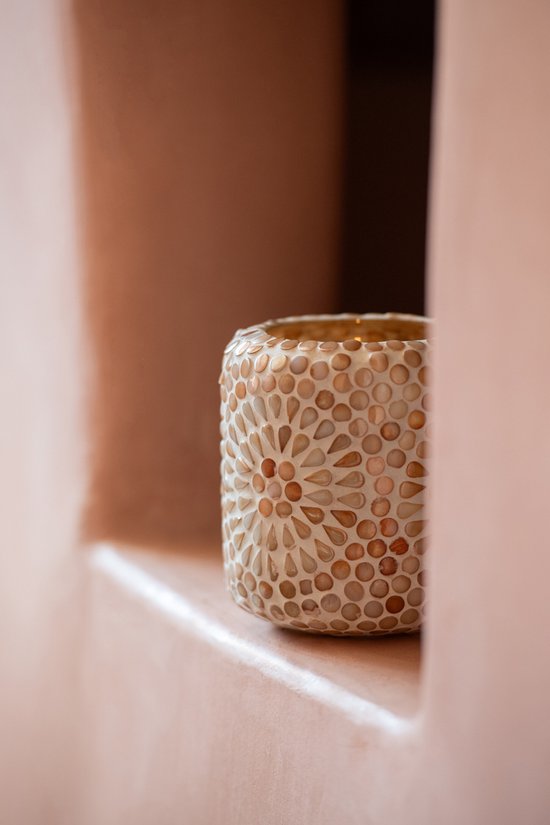 Cilindrische kaarsenhouder met beige en witte mozaïektegels in een bloemenpatroon, staand op een roze richel.