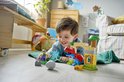 Een jongetje speelt op de grond met LEGO Duplo blokken, waaronder een rode en blauwe dinosaurus, groene goblin en een fort.